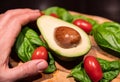 A wooden cutting board on a black background with an avocado in the center. All around, intense green basil leaves and bright red Royalty Free Stock Photo