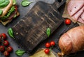 Wooden cutting board on dark background witn delicious sandwich, ham, bacon, cheese, spices, tomatoes, sausage, gammon, herb. Meat Royalty Free Stock Photo