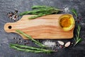 Wooden cutting board, olive oil, rosemary plant, salt, garlic and pepper on black table from above for food cooking background or