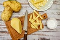 Wooden cutting board with a potato cut into a stick shape to make French fries. Half a peeled potato and a knife on a rustic table Royalty Free Stock Photo