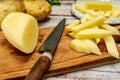 Wooden cutting board with a potato cut into a stick shape to make French fries. Half a peeled potato and a knife on a rustic table Royalty Free Stock Photo