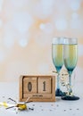 A wooden date block with January first on it with flute glasses of champagne.