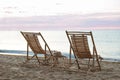 Wooden deck chairs and wicker table on sandy beach at sunset. Summer vacation Royalty Free Stock Photo