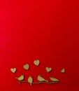 Wooden decoration flock of enamored birds sitting on a branch and wooden hearts around birds on a red background. Copy space.