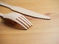 Wooden degradable fork and knife on a light wood table surface,