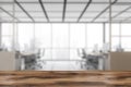 Wooden desk on foreground, blurred white office room with computers near window