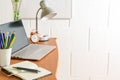 Wooden desk with laptop, notebook, pencils, lamp and tools against a rough white wall, small home office, copy space, selected