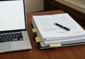 A wooden desk with a laptop and a stack of documents. The laptop Royalty Free Stock Photo