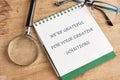 On a wooden desk, a notepad with the message expressing gratitude for creative solutions is highlighted, alongside a