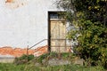 Wooden dilapidated entrance doors to abandoned ruins of suburban family house with broken steps and rusted metal fence