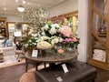 A wooden dining table and wicker chair with floral display at a Pottery Barn at an indoor mall in Orlando, Florida