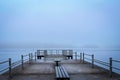 Wooden dock with benches on the sea covered in the fog in the morning