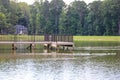 A wooden dock with a black rod iron railing in the middle of silky green still lake water surrounded by lush green trees and grass Royalty Free Stock Photo