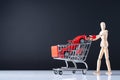 A wooden doll carries a red car model in metal shopping cart. Royalty Free Stock Photo