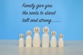Wooden doll figures standing with phrase FAMILY GIVE YOU THE ROOTS TO STAND TALL AND STRONG