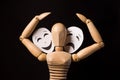 Wooden doll on hinges holds a mask in hands and covers her face on a black background Royalty Free Stock Photo