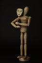 Wooden doll on hinges holds a mask in hands and covers her face on a black background Royalty Free Stock Photo