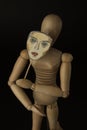 Wooden doll on hinges holds a mask in hands and covers her face on a black background Royalty Free Stock Photo