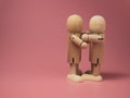 2 wooden dolls hugging each other on a pink background. Concept of social contact from wooden dolls