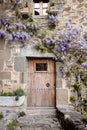 Wooden door in old medieval stone house, purple wisteria in blossom on the house over the door, Rupit, Spain. Magic house from won