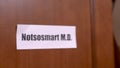 Wooden door opens to the office of quack doctor, on which hangs sign with funny name, close up, blurred background