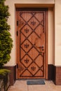 Wooden door with tree beside. Carved brown door with doormat. Entrance to house. Royalty Free Stock Photo