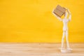 wooden dummy figure holding present box over yellow background. Royalty Free Stock Photo