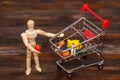 Wooden dummy puppet with mini shopping cart. Abstract food concept