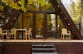 Wooden dwelling in the form of a hut with fallen leaves on the terrace. Trees are beautifully reflected in the glass.