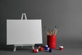 Wooden easel with blank canvas board and painting tools for children on dark background.