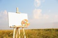 Wooden easel with blank canvas and painting equipment in field. Space for text Royalty Free Stock Photo