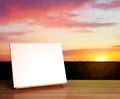 Wooden easel with blank canvas on table and field at sunset. Space for text