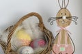 A wooden Easter bunny near a wicker basket with three crocheted eggs in front of a bright background Royalty Free Stock Photo