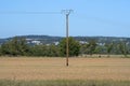 A wooden electric pole standing in the middle of a plowed field, in the background hills with trees. Royalty Free Stock Photo