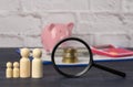 Wooden family figurines and  pink ceramic piggy bank on blue background. Concept of accumulating cash for buying a house and a car Royalty Free Stock Photo