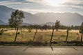 Wooden fence with barbed wire with a road in the foreground and a field, trees, and mountains in the background on a sunny Royalty Free Stock Photo