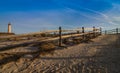 Wooden fence leads to beach near lighthouse in Cape May, NJ, on a sunny morning