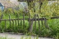 A wooden fence is overgrown with grass and collapses near an abandoned house