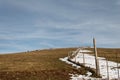 Wooden fence posts and barbed wire marking the property line of a prairie with dried grass and patches of snow under Royalty Free Stock Photo