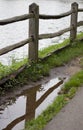 Portrait image of wooden fence by lake reflected in puddle Royalty Free Stock Photo