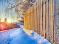 Wooden fence, snowy road, sunset or sunrise on background. Beautiful winter landscape