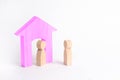 A wooden figure of a man meets a guest on a white background. Pink house. The concept of an apartment house, real estate. Royalty Free Stock Photo