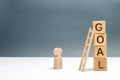 The wooden figure of a man stands near a tower of cubes with the word goal. The concept of achieving the goal, dedication