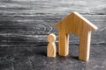 A wooden figure of a man stands near a wooden house on a gray concrete background. Concept of real estate, renting and buying