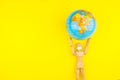 Wooden figure mannequin carrying planet earth globe over head on a yellow background Royalty Free Stock Photo