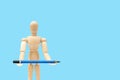 Wooden figure mannequin holding blue pencil in hand.