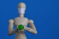 Wooden figure of a mannequin in a medical mask holding a green pill on a blue background. Coronavirus, pandemic and Royalty Free Stock Photo