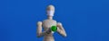 Wooden figure of a mannequin in a medical mask holding a green pill on a blue background. Coronavirus, pandemic and Royalty Free Stock Photo