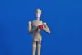 Wooden figure of a mannequin in a medical mask holding a red pill on a blue background. Coronavirus, pandemic and Royalty Free Stock Photo