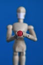 Wooden figure of a mannequin in a medical mask holding a red pill on a blue background. Coronavirus, pandemic and Royalty Free Stock Photo